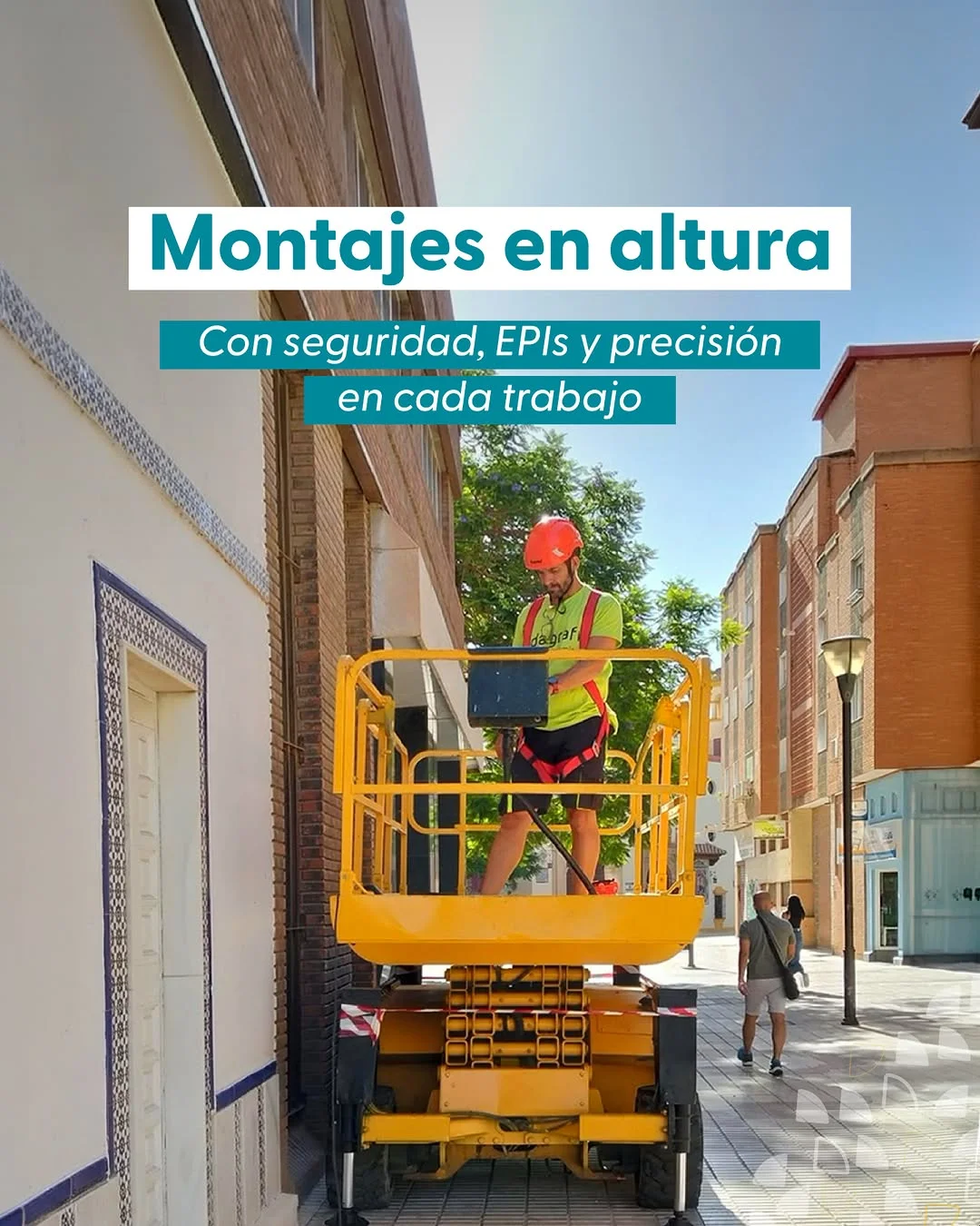 Operario de Indagrafic en plataforma elevadora amarilla instalando rotulación en altura en fachada de calle de Málaga, con casco y chaleco de seguridad