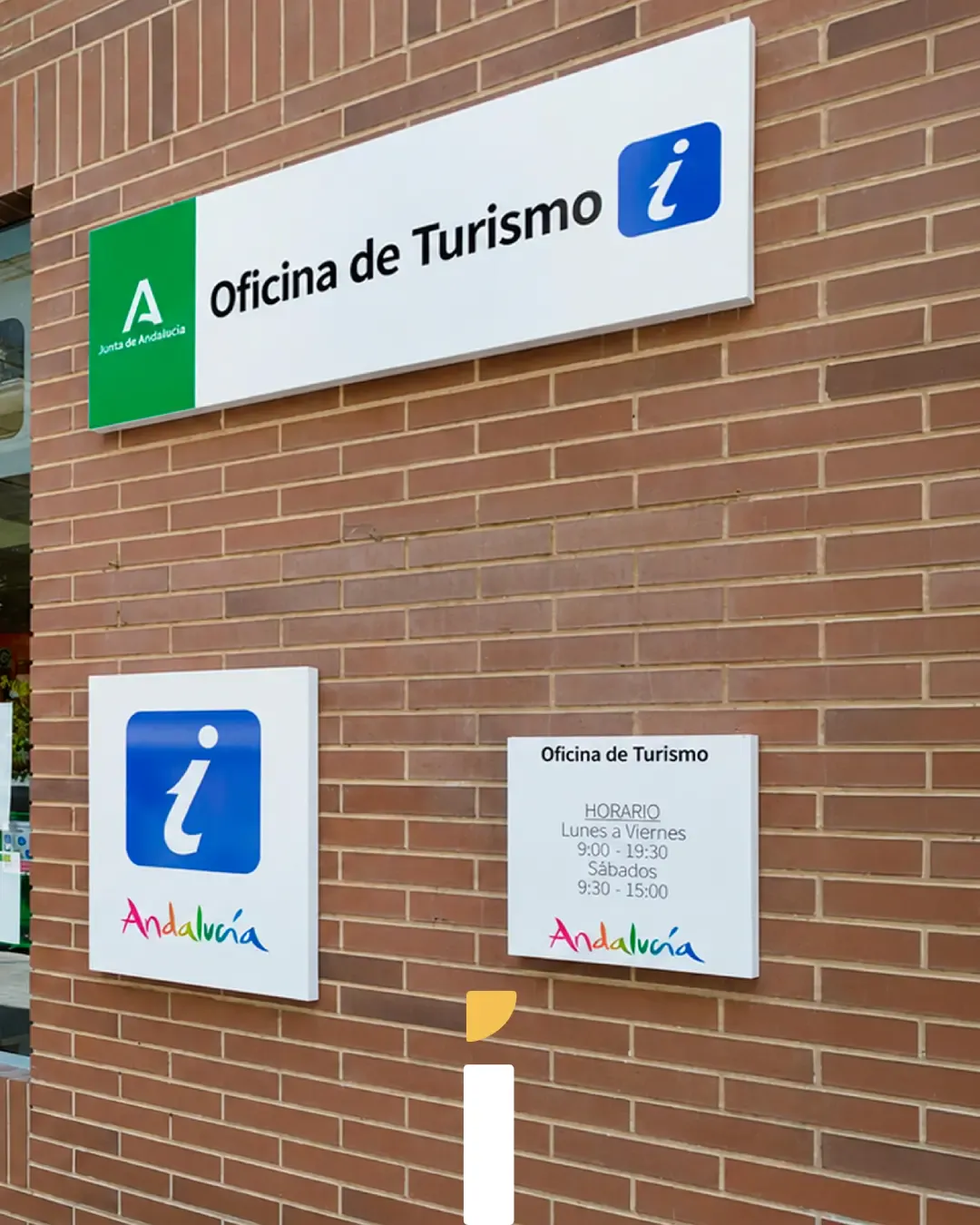 Rotulación en Andalucía: cartel de Oficina de Turismo con placa de horarios sobre fachada de ladrillo