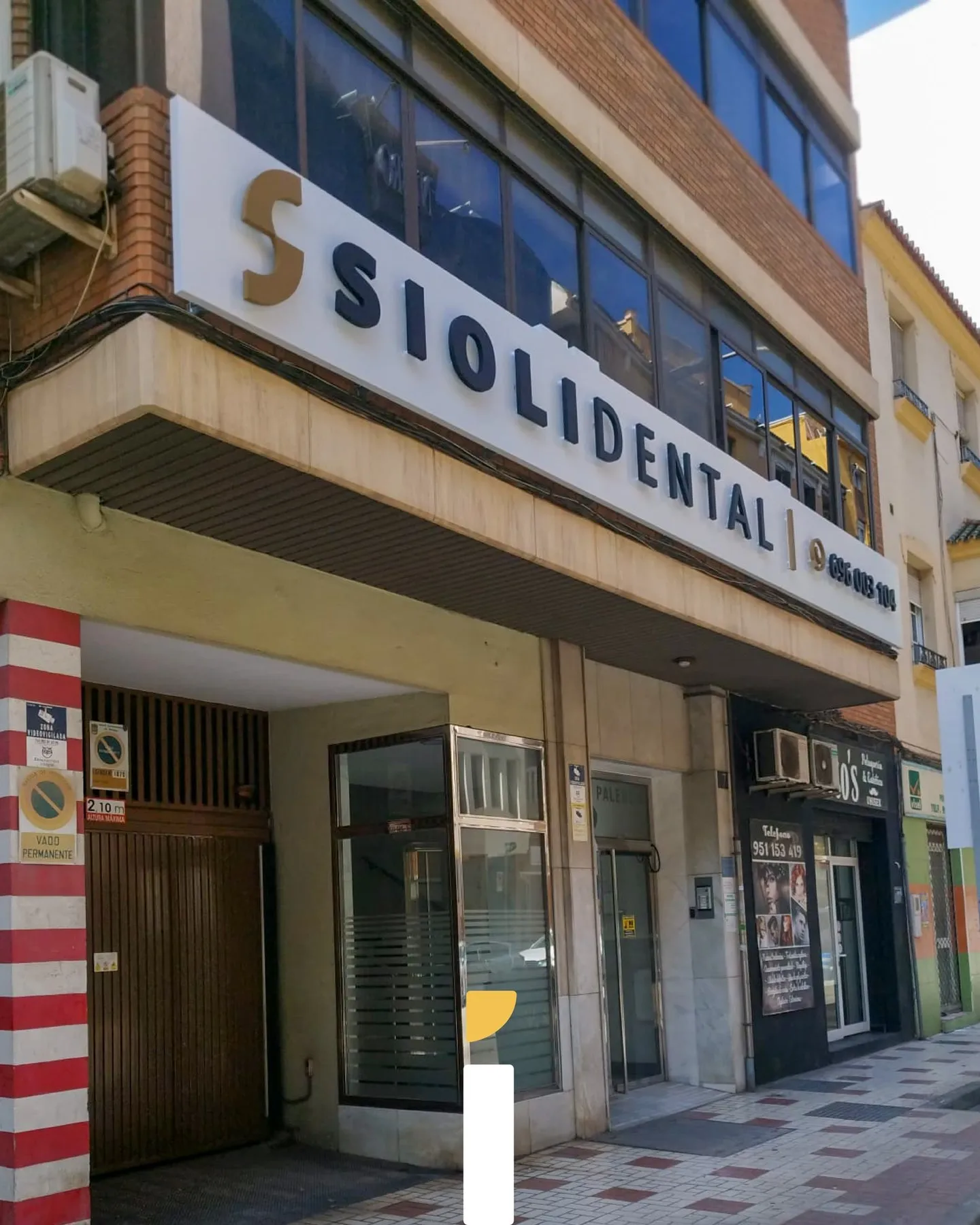 Rótulo de Siolidental visto de día en escorzo, con letras cajeadas lacadas en mate sobre panel blanco